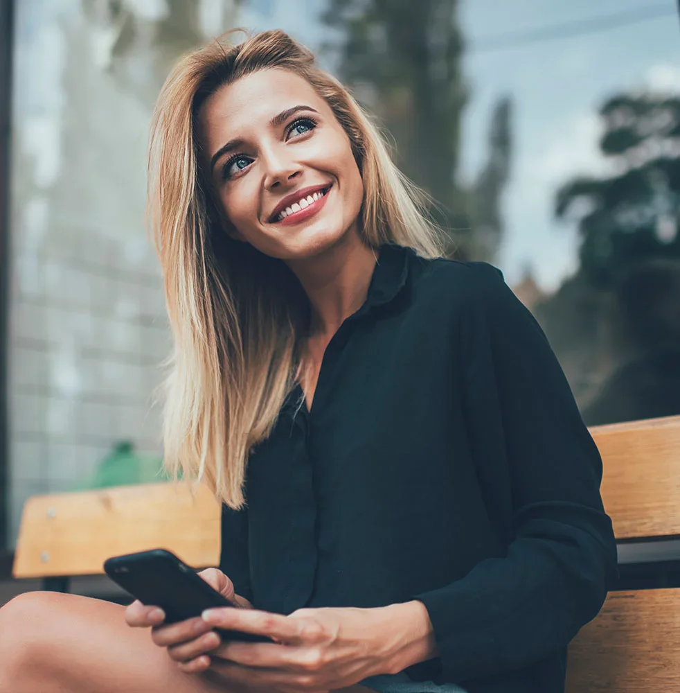 Blonde woman in black sitting on a park bench with her phone | Fat Grafting in Orlando